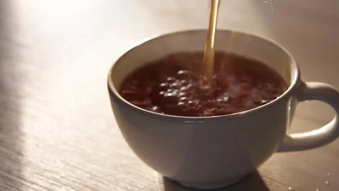 Pouring hot black tea into a white cup on a wooden table. Steam. Stock Footage