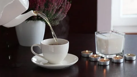 Pouring hot black tea in white ceramic cup with lighted scented candles around Stock Footage 252101040