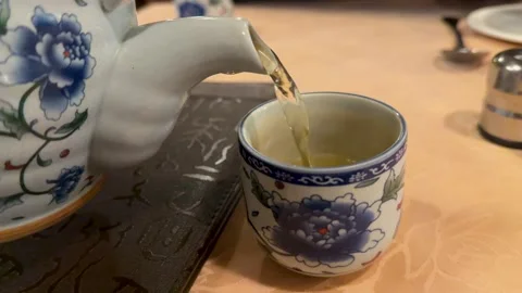 Pouring Hot Green Tea from Ceramic Teapot into Cup Stock Footage 345714853