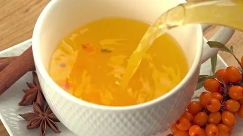 Pouring hot healthy fruit tea from sea buckthorn from a teapot into a cup with Stock Footage 213983699