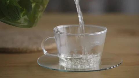 Pouring hot mint tea into transparent glass tea cup. Stock Footage 160832612