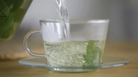 Pouring hot mint tea into transparent glass tea cup. Stock Footage 160832692
