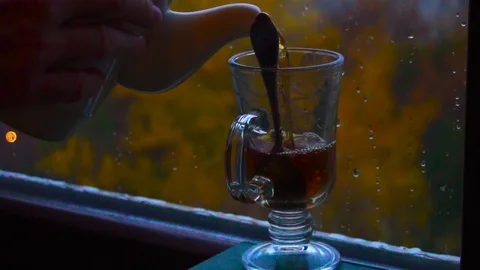Pouring hot tea into a cup in front of the window in autumn. Close-up Stock Footage 100408942