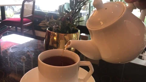 Pouring hot tea from a white teapot to a white cup on a table Stock Footage 203663900