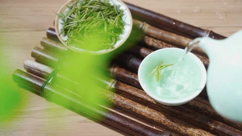 Pouring Hot Water into Ceramic Teacup on Bamboo Tray with Green Tea Leaves Stock Footage 339639454
