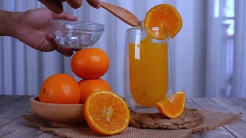 Pouring ice cube into fresh orange juice with orange slices as garnish Stock Footage 268384251