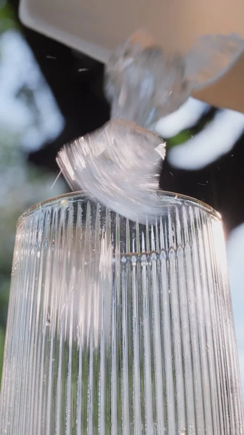 Pouring ice cubes into a glass. Refreshing drink preparation outdoors. Vertical Stock Footage 316169306