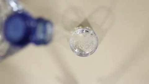Pouring liquid from a bottle into a clear container on a flat surface in a brigh 库存影片 325032720