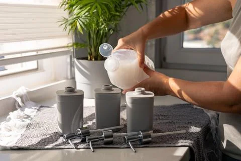 Pouring liquid into gray containers on a kitchen countertop with plants in the Stock Photos