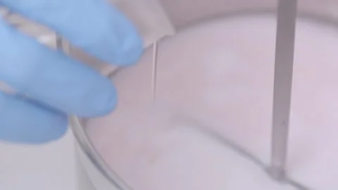 Pouring liquid into a light pink mixture in a container, laboratory Stock Footage 338424043
