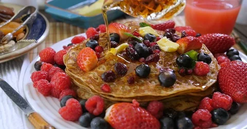 Pouring maple syrup over a breakfast of pancakes with berries and dry fruits Stock Footage 73137622