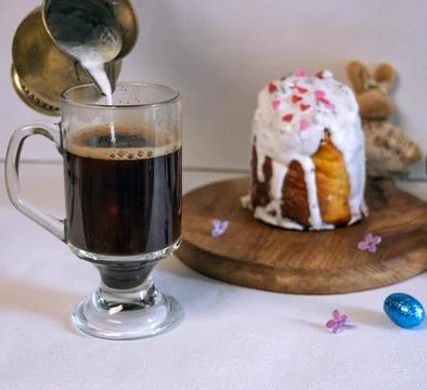 Pouring milk into coffee with Easter cake and plush bunny on background. 库存照片