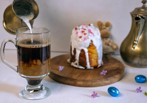 Pouring milk into coffee with Easter cake and plush bunny on background. Фото
