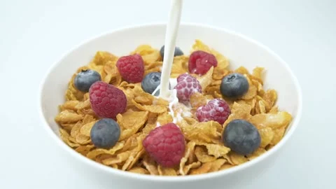Pouring milk on corn flakes cereals with raspberry and blueberries in a bowl Stock Footage 233168319