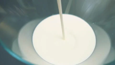 Pouring milky white liquid into a deep glass bowl indoors Vidéo 342880546