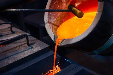 Pouring molten metal from a ladle into a rectangular graphite mold. Stock Photos