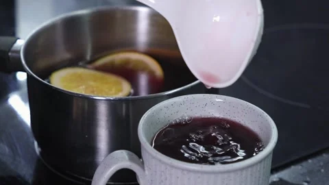 Pouring mulled wine from ladle into ceramic mug with orange slices in saucepa Stock Footage 292908281