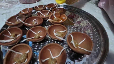 Pouring oil and ghee in earthen oil lamps by a female asian woman Stock Footage 290155489