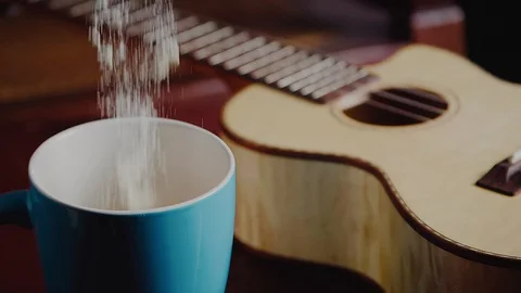 Pouring powdered milk in cup beside my guitar at my home den, slow motion Stock Footage 128819839