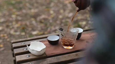 Pouring pu-erh tea from a clay teapot into a glass cup. outdoors tea ceremony Stock Footage 229860861