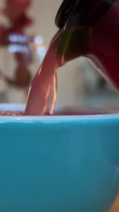 Pouring raspberry tea from glass teapot into blue cup of stream of hot drink in Stock Footage 256894041