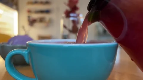 Pouring raspberry tea from glass teapot into blue cup of stream of hot drink in Stock Footage 256894055