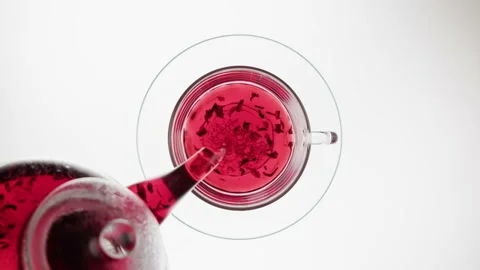 Pouring red fruit tea in cup top view. Freshly brewed hibiscus tea on white Stock Footage 196118639