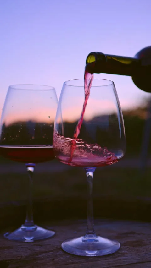 Pouring red wine into glasses at sunset on a wooden barrel Stock Footage 252610403