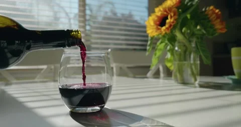Pouring Red Wine on a Table with Sunlight Through Blinds and Sunflowers Stock Footage 313778388