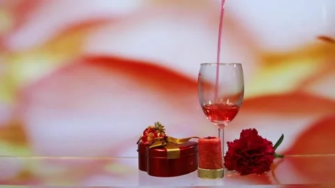 Pouring red wine into two glasses, carnation flower with colourful rosy backg Stock Footage 151626019