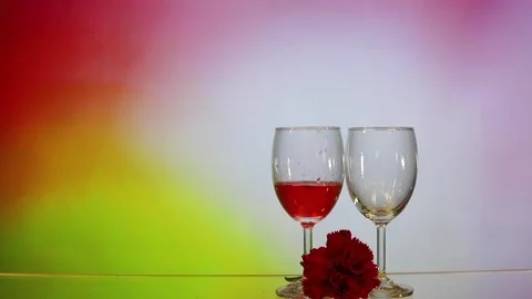 Pouring red wine into two glasses, carnation flower with colourful rosy backg Stock Footage 151626023