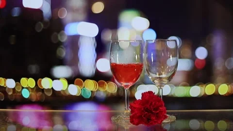 Pouring red wine into two glasses, carnation flower with colourful blurred ci Stock Footage 151626033