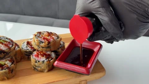 Pouring soy sauce beside crispy fried sushi rolls on wooden serving board at Stock Footage 346185901