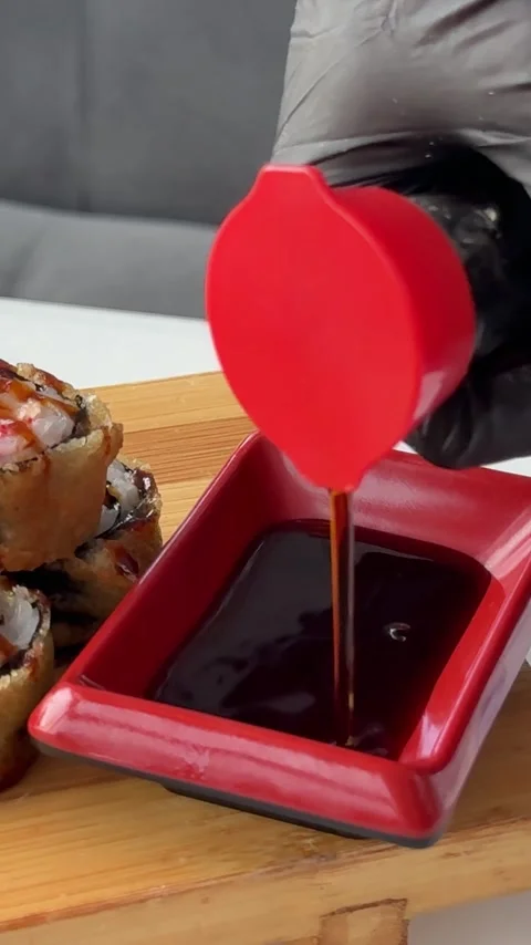 Pouring soy sauce beside crispy fried sushi rolls on wooden serving board at Stock Footage 346186027