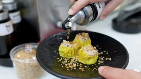 Pouring Soy Sauce Over Steamed Shumai Dumplings on a Black Plate Stock Footage 334092003