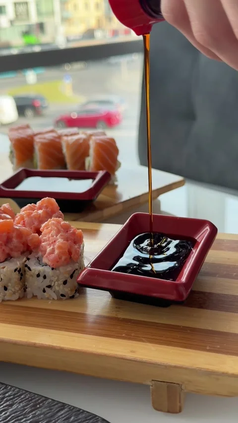 Pouring soy sauce into red rectangular dish beside salmon sushi rolls with Stock Footage 346185850
