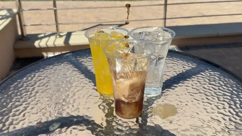 Pouring sparkling cola into a plastic cup beside water and lemonade on a sunny Stock Footage 345178963
