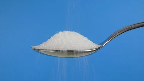Pouring sugar into a silver spoon against a blue background Stock Footage 325037685