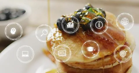 Pouring syrup over stack of pancakes on counter, with blueberries, pistachios Stock Photos