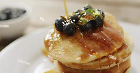 Pouring syrup over three-layer pancake stack on kitchen table, with blueberries Stock Photos