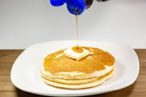 Pouring syrup onto the square of butter on a stack of golden pancakes Stock Photos
