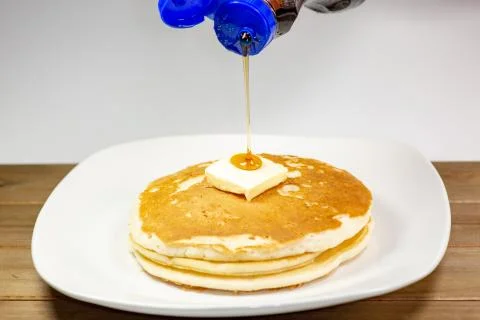 Pouring syrup onto the square of butter on a stack of golden pancakes Stock Photos