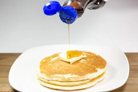 Pouring syrup onto the square of butter on a stack of golden pancakes Stock Photos