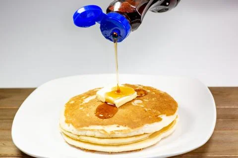 Pouring syrup onto the square of butter on a stack of golden pancakes Stock Photos
