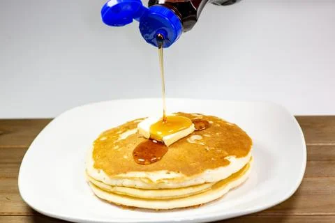 Pouring syrup onto the square of butter on a stack of golden pancakes Stock Photos