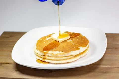 Pouring syrup onto the square of butter on a stack of golden pancakes Stock Photos