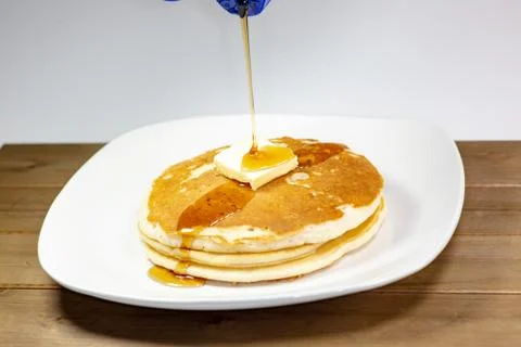 Pouring syrup onto the square of butter on a stack of golden pancakes Foto stock