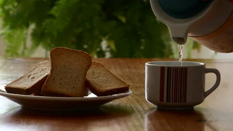 Pouring tea into a cup, next to a plate of toast Stock Footage 230465072