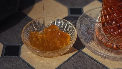 Pouring thick sweet watermelon jam into a crystal bowl next to tea Stock Footage 344901059