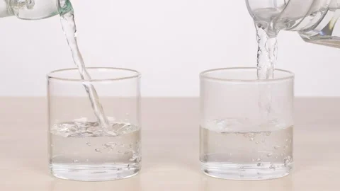 Pouring Water Into Two Glasses on a Tabletop Stock Footage 318943126